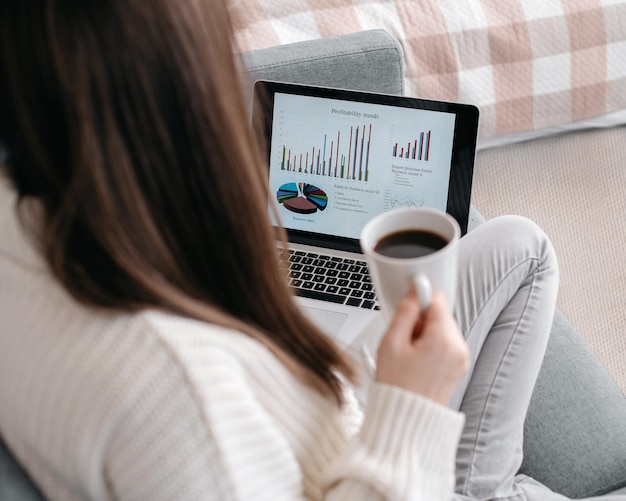 Young woman with a laptop is drinking coffee in her bedroom