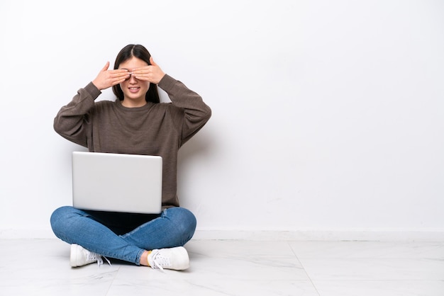 Young woman with a laptop sitting on the floor covering eyes by hands