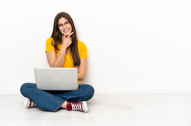 Young woman with a laptop sitting on the floor smiling