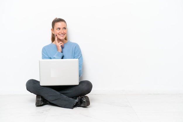 Young woman with a laptop sitting on the floor thinking an idea while looking up