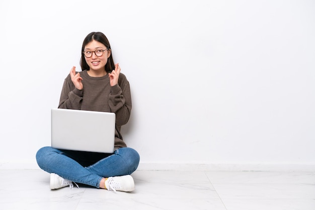 Young woman with a laptop sitting on the floor with fingers crossing