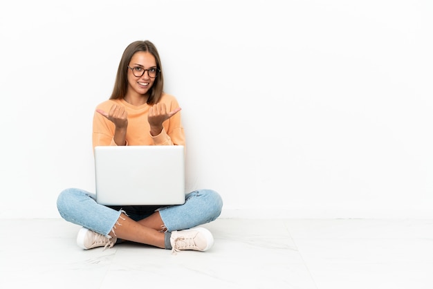 Young woman with a laptop sitting on the floor with thumbs up gesture and smiling