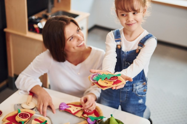 Young woman with little girl playing with toys together on the kitchen