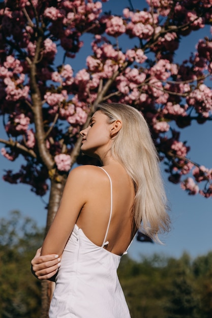 Young woman with long blonde hair outdoors in a park on cherry tree in bloom background