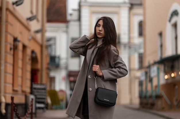 young woman with long brown hair in a fashionable coat posing in the city