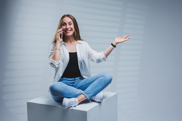 Young woman with long brunette hair wearing a white shirt and jeans talking on the phone A woman in jeans and a plain white shirt with a mobile phone White background copy space