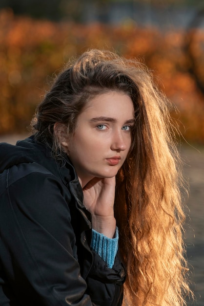 Young woman with long chestnut thick curly hair looks into the camera Girl with auburn wavy hair