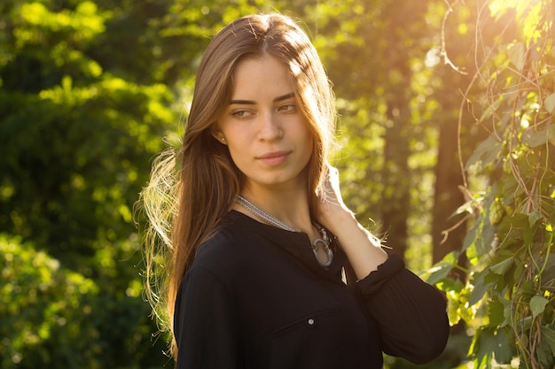 Young woman with long hair in black blouse and silver necklace on the background of green trees