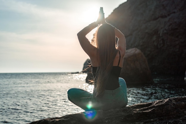 Young woman with long hair in black swimsuit and boho style braclets practicing outdoors on yoga mat