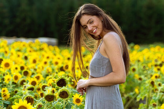 Young woman with long hair in linean country style dress walks through a field of sunflowers