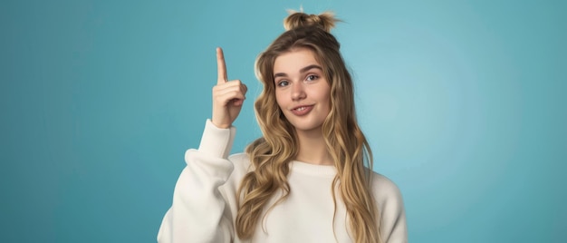 A young woman with long hair smiles confidently raising her finger against a solid blue background