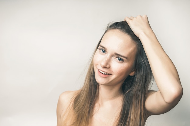 Young woman with long hair smiles, looks at the camera, strokes her hair with her hand