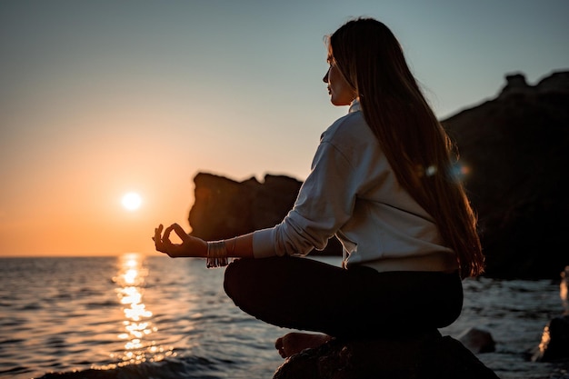 Young woman with long hair in sportswear and boho style braclets practicing outdoors on yoga mat by the sea on a sunset Women's yoga fitness routine Healthy lifestyle harmony and meditation