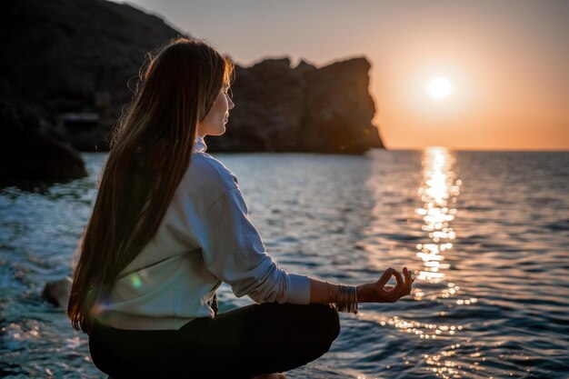 Young woman with long hair in sportswear and boho style braclets practicing outdoors on yoga mat by