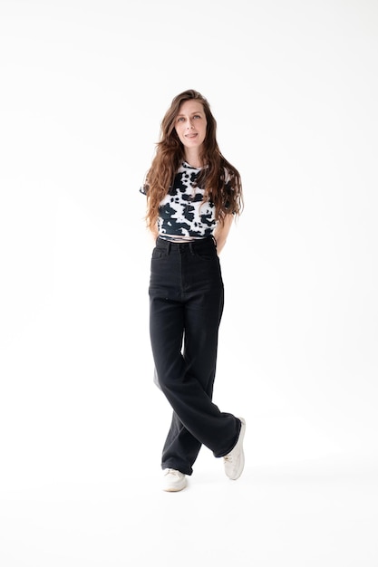 Young woman with long hair in a spotted Tshirt jeans and braces poses while standing in the studio