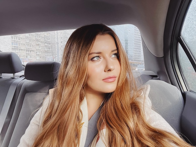 Young woman with long hair wavy hairstyle in the car or taxi cab as passenger exploring the city transport and travel