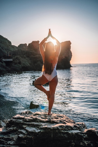 Young woman with long hair in white swimsuit and boho style braclets practicing outdoors on yoga mat