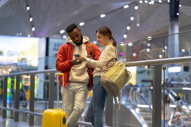 Young woman with mobile phone helping african man traveler in airport showing direction on map