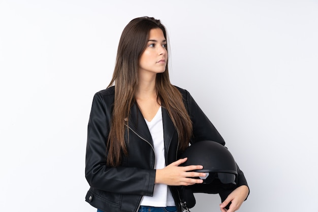 Young woman with a motorcycle helmet over isolated white wall looking side