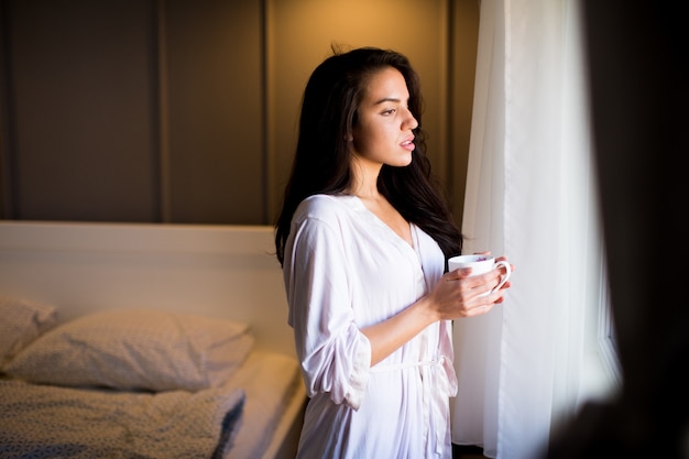 Young woman with mug in bedroom