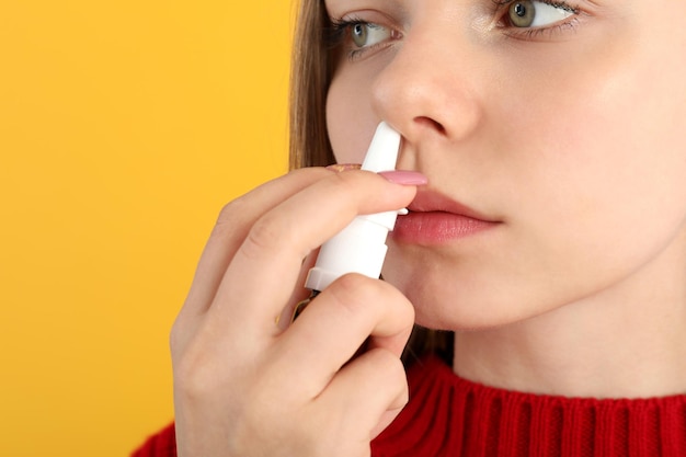 Young woman with nasal drops on yellow background, runny nose concept