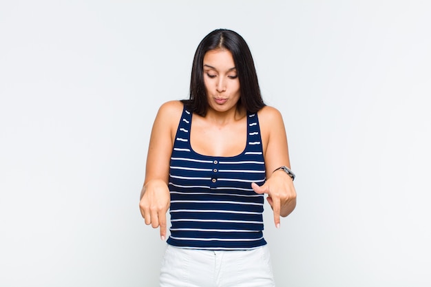 Young woman with open mouth pointing downwards with both hands, looking shocked, amazed and surprised