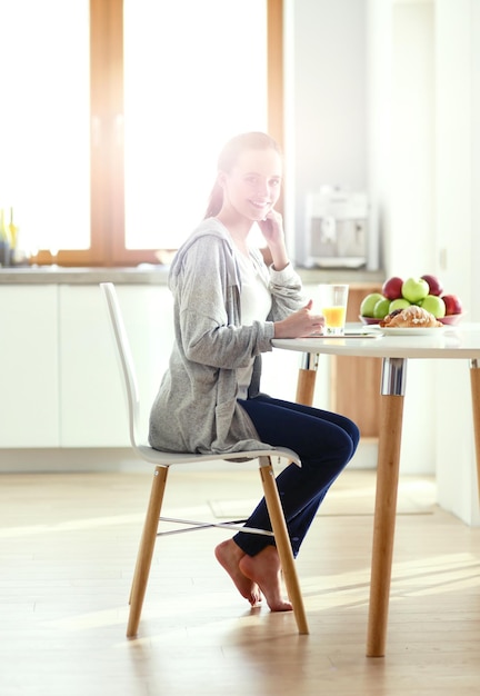 Young woman with orange juice and tablet in kitchen