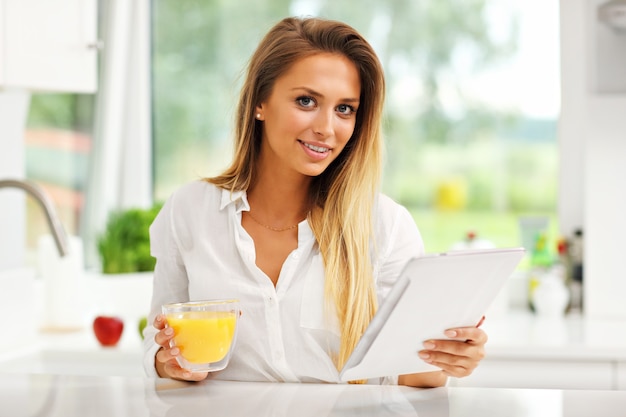 young woman with orange juice and tablet in kitchen