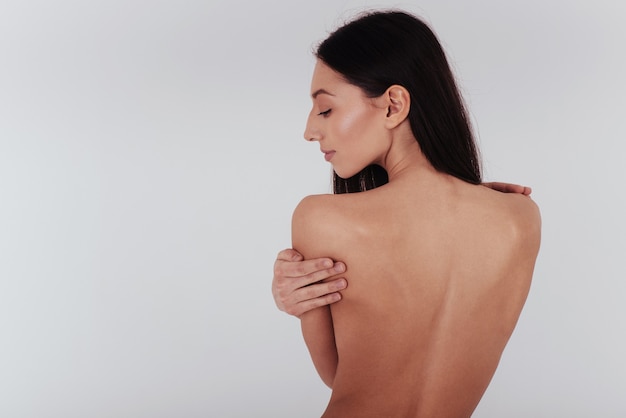 Young woman with perfect body and smooth skin stands with her back on the white wall.