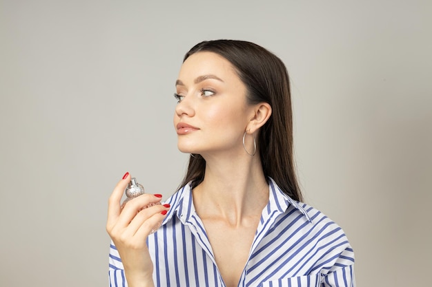 Young woman with perfume bottle in hand on white background