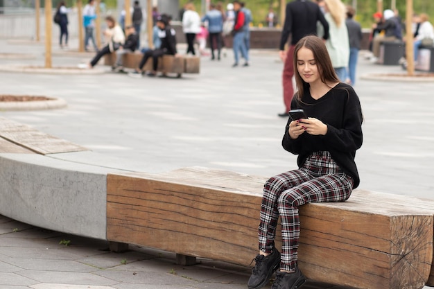 Young woman with a phone on the street on a bench smiles