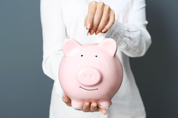 Young woman with piggy bank on color background