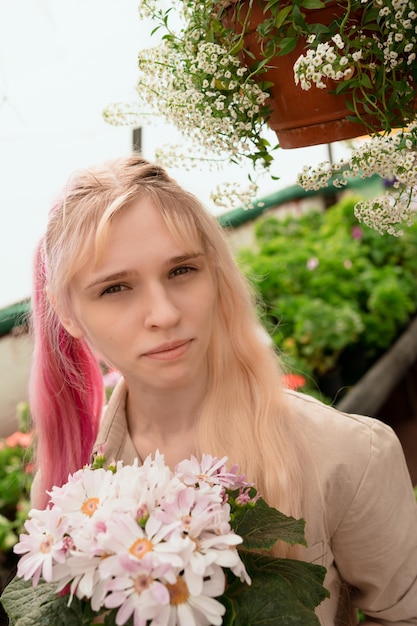 Young woman with pink and blond hair holding pink flowers in garden