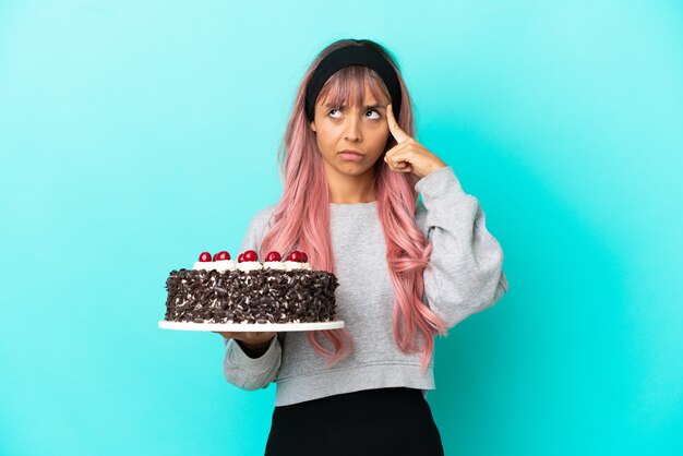 Young woman with pink hair holding birthday cake isolated on blue background thinking an idea