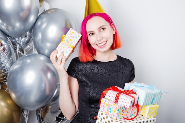 young woman with pink hair and party hat holds birthday gifts and smiles