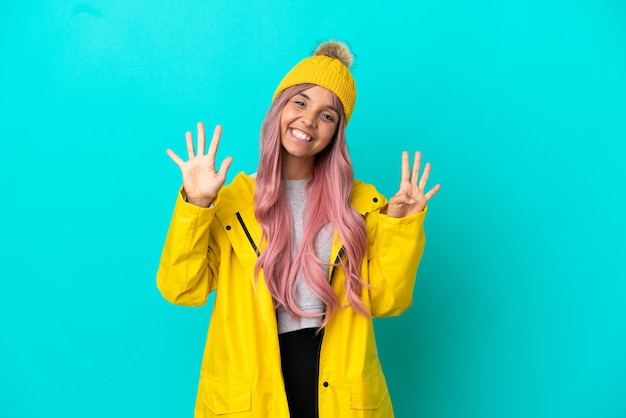 Young woman with pink hair wearing a rainproof coat isolated on blue background counting nine with fingers