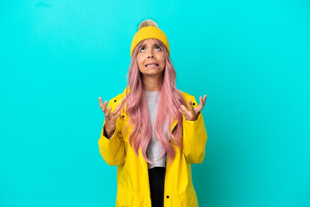 Young woman with pink hair wearing a rainproof coat isolated on blue background stressed overwhelmed