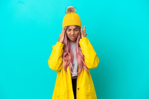 Young woman with pink hair wearing a rainproof coat isolated on blue background with headache