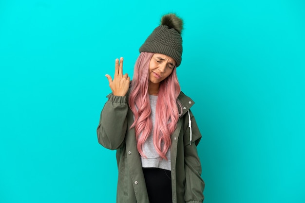 Young woman with pink hair wearing a rainproof coat isolated on blue background with problems making suicide gesture