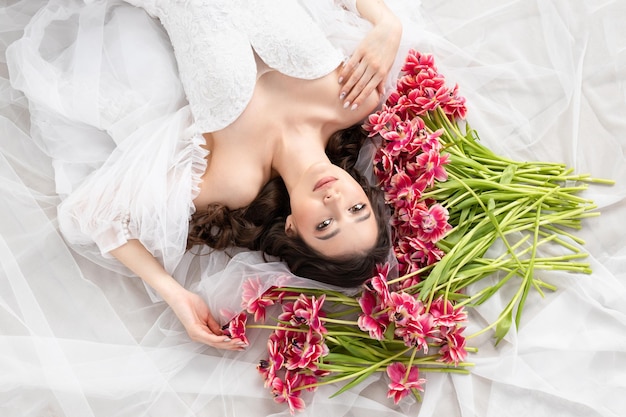 Young woman with pink tulips in hands white dress