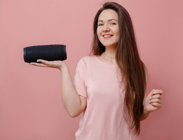 Young woman with a portable loudspeaker in hand on pink background