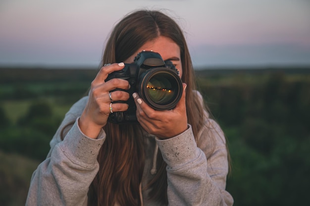 A young woman with a professional camera takes a photo in nature.