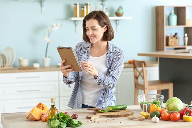 Young woman with recipe book cooking in kitchen