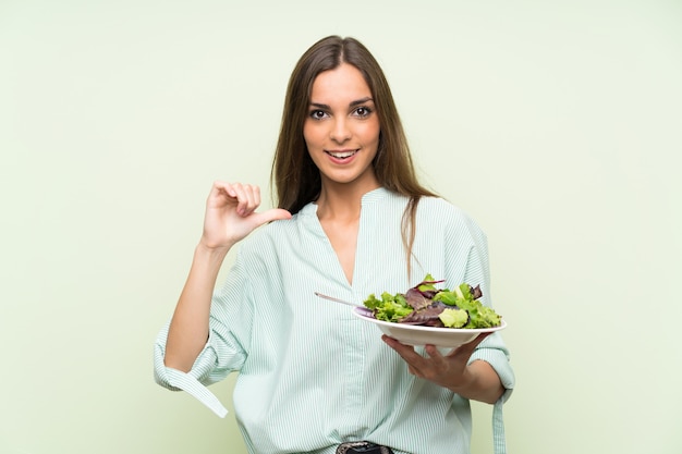 Young woman with salad over isolated green wall proud and self-satisfied