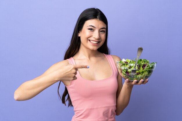 Young woman with salad over purple wall