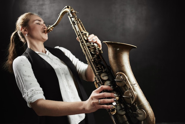 Young woman with saxophone on black background