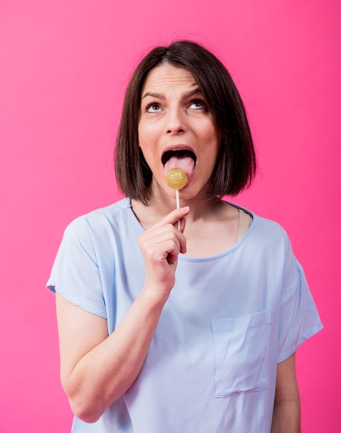 Young woman with sensitive teeth eating sweet lollipop on color background