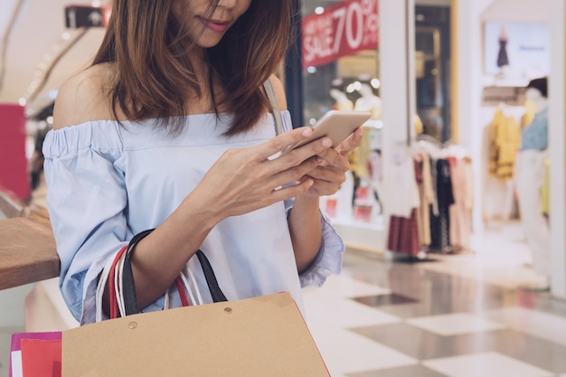 Young woman with shopping bags using smart phone and shopping in the mall