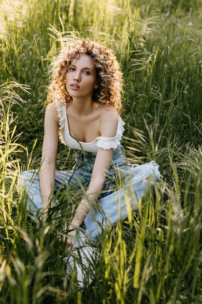 Young woman with short curly hair sitting in a field with tall green grass