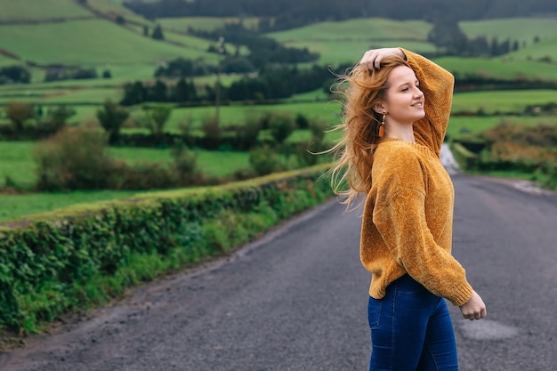 A young woman with short hair stands on the road along a green field Ecological tourism concept